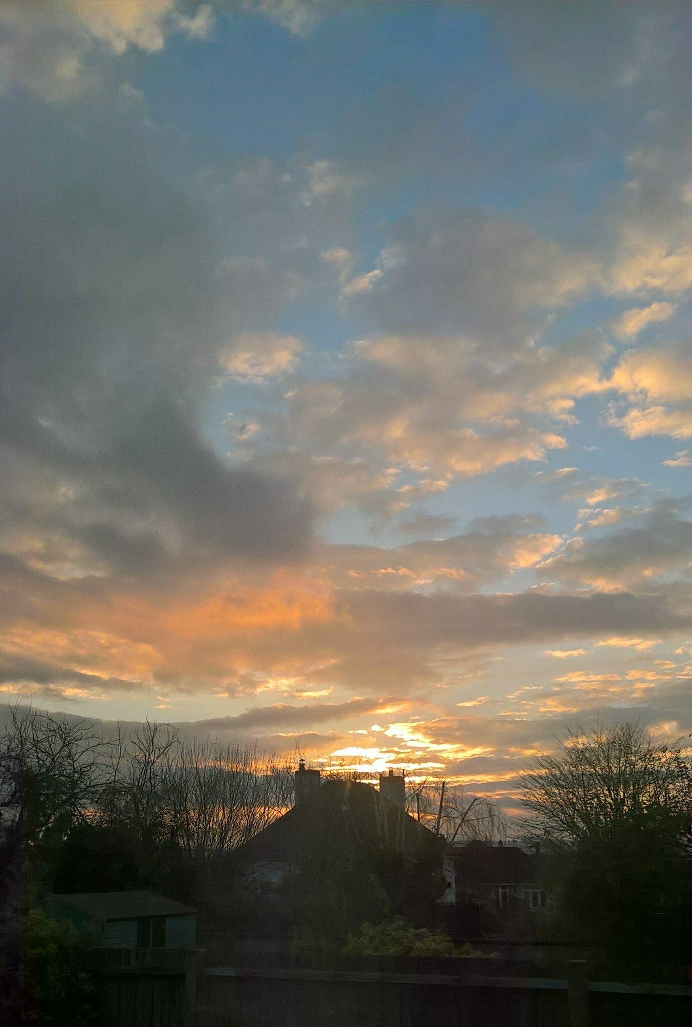 Auto-generated description: A beautiful sunset with vibrant clouds above silhouetted houses and trees.