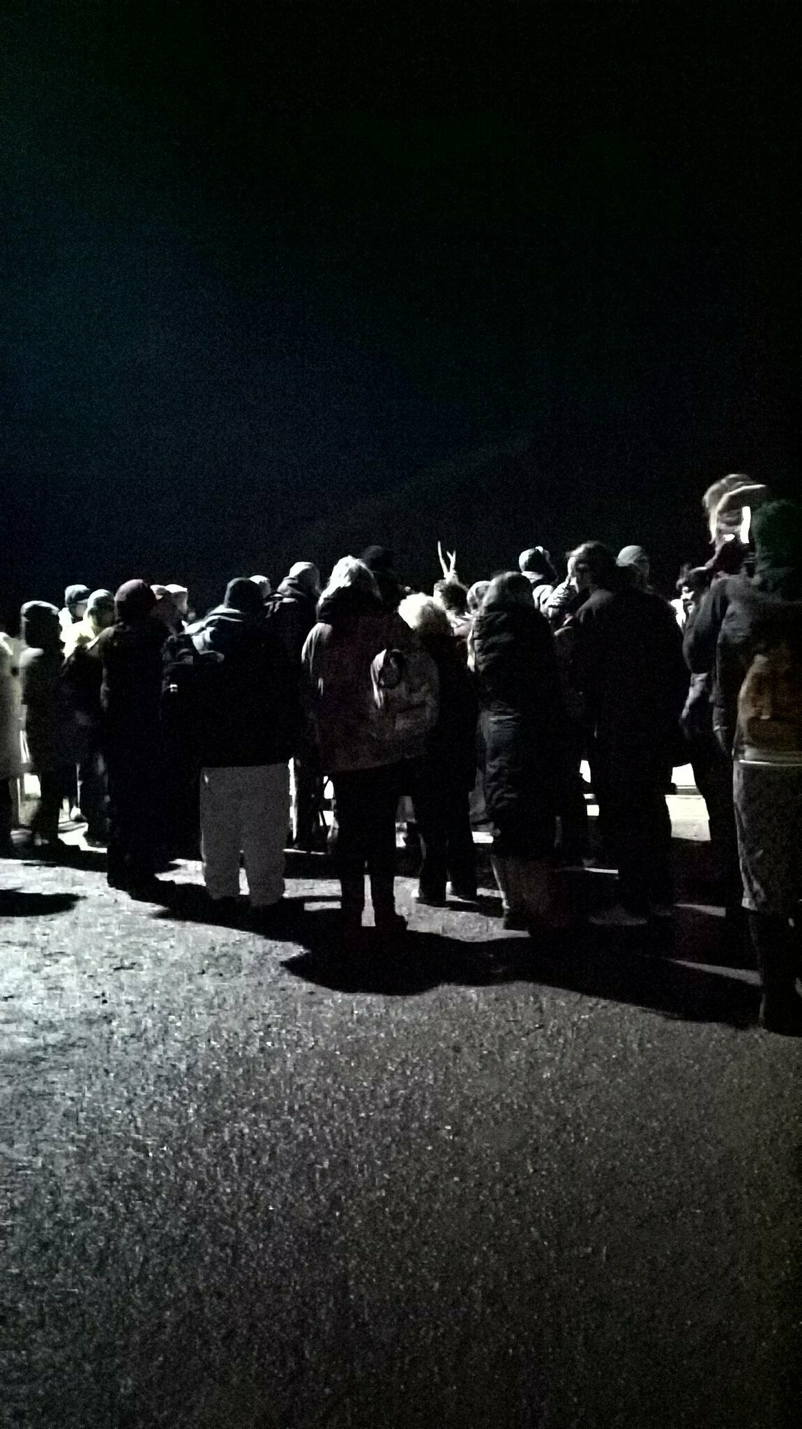 Auto-generated description: A group of people stands together in the dark, possibly observing something.