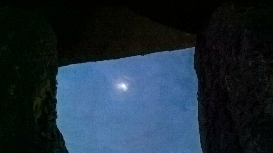 Auto-generated description: A view of the night sky with a bright moon is framed by large rock formations, creating a natural window-like opening.