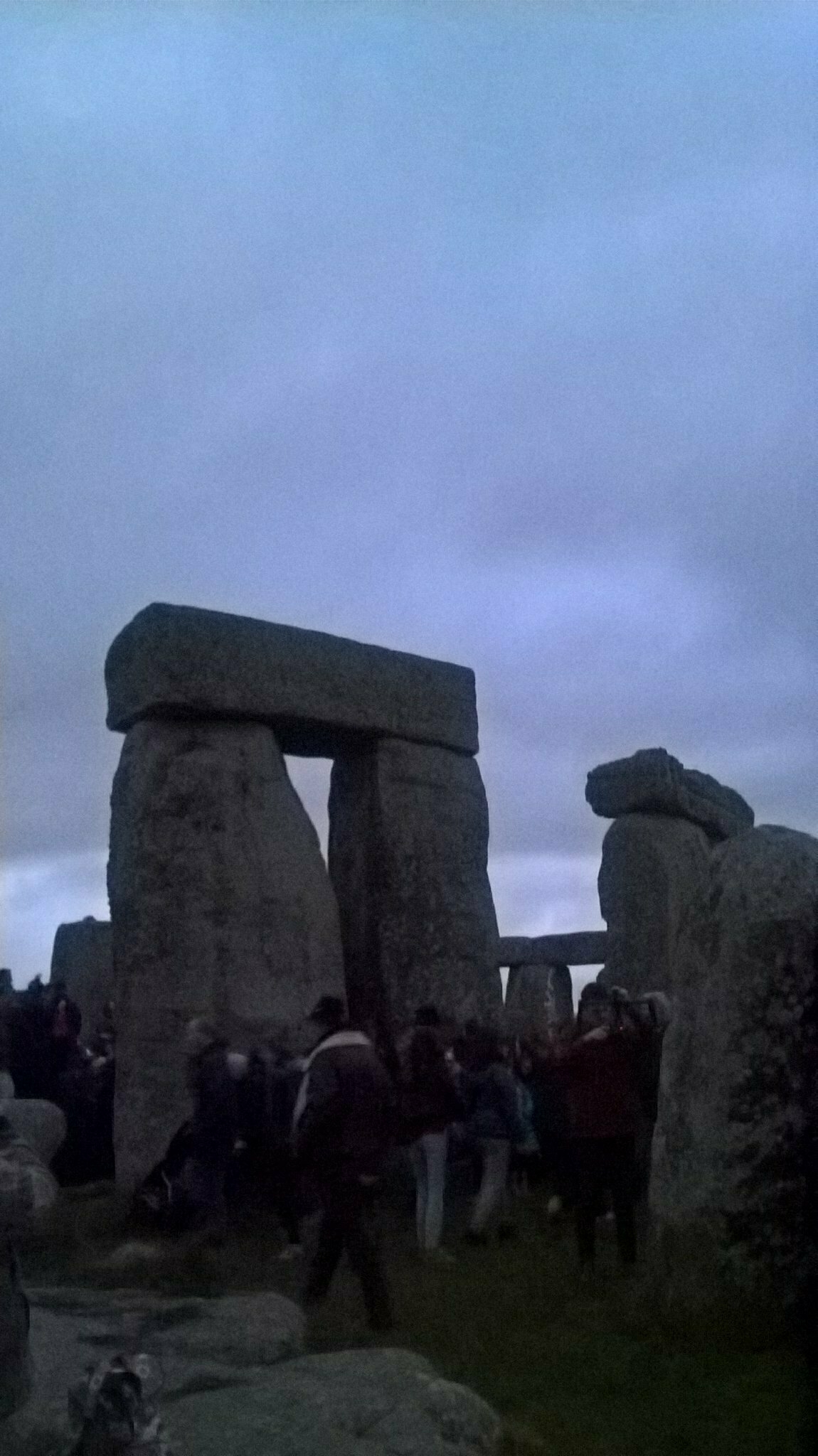 Auto-generated description: People are gathered around the stone structures of Stonehenge under a cloudy sky.