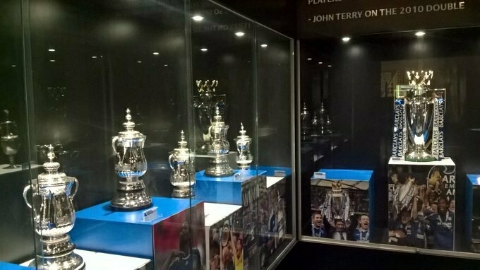 Auto-generated description: Multiple football trophies are displayed in glass cases, including the Premier League trophy.