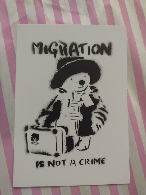 Auto-generated description: A stencil artwork depicts a bear holding a suitcase with the text MIGRATION IS NOT A CRIME above and below it.