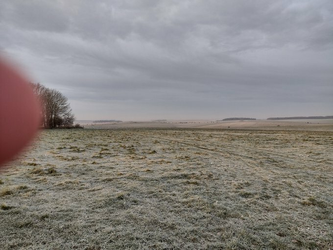 Auto-generated description: A frosty field on a cloudy day is partially obscured by a finger in the corner.