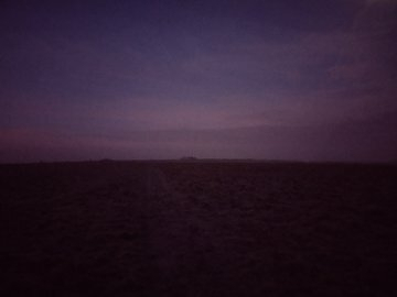 Auto-generated description: A dark, empty landscape stretches out under a twilight sky with shades of purple and pink.