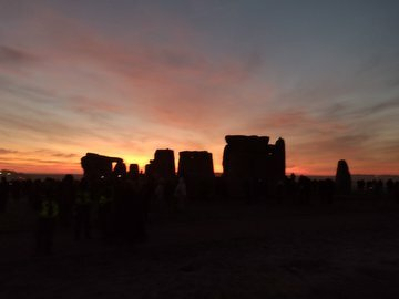 Auto-generated description: Silhouetted against a vibrant sunrise or sunset sky, large standing stones create an iconic megalithic scene.