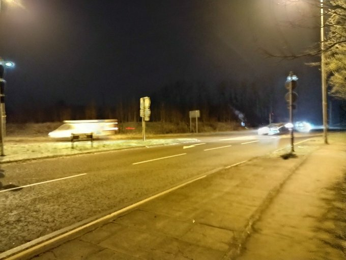 Auto-generated description: A dimly lit street at night features a few passing cars leaving motion blur on the wet road.