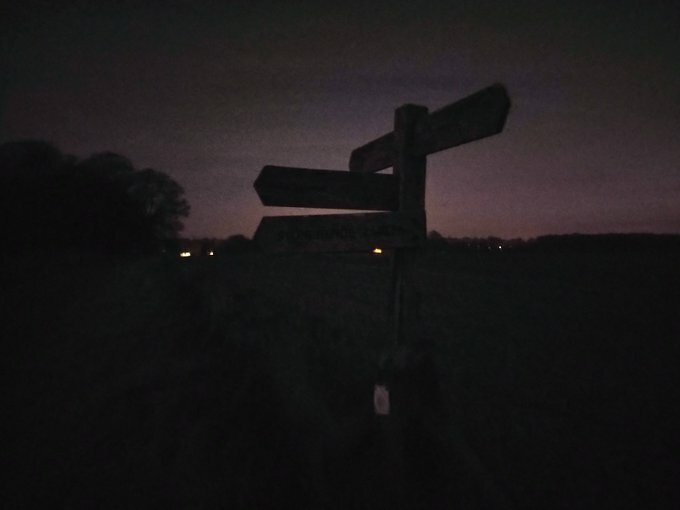 Auto-generated description: A silhouetted signpost stands against a dark twilight sky with faint outlines of trees in the background.