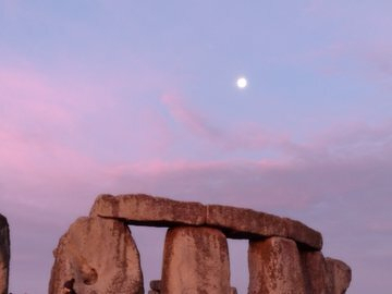 Auto-generated description: Stonehenge stands against a pinkish sky with the moon visible above.