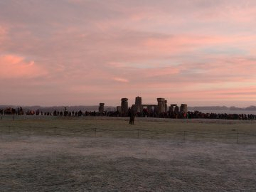 Auto-generated description: A large crowd gathers near the ancient stone structure of Stonehenge under a colorful sunset sky.